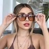 A woman models vintage square sunglasses with a double bridge against a bright background.