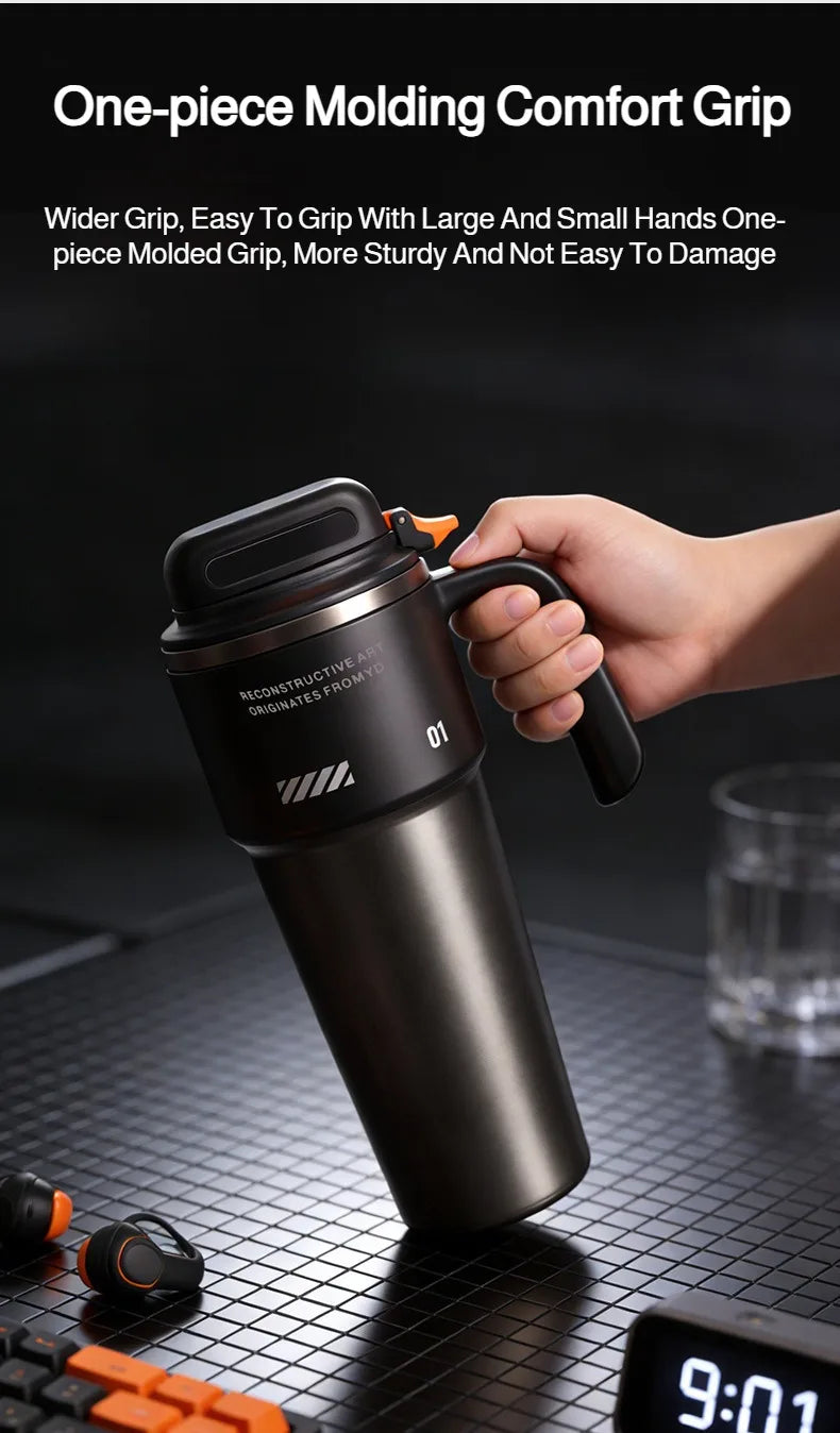 A hand holds a black insulated stainless steel tumbler with a handle and straw on a dark surface.
