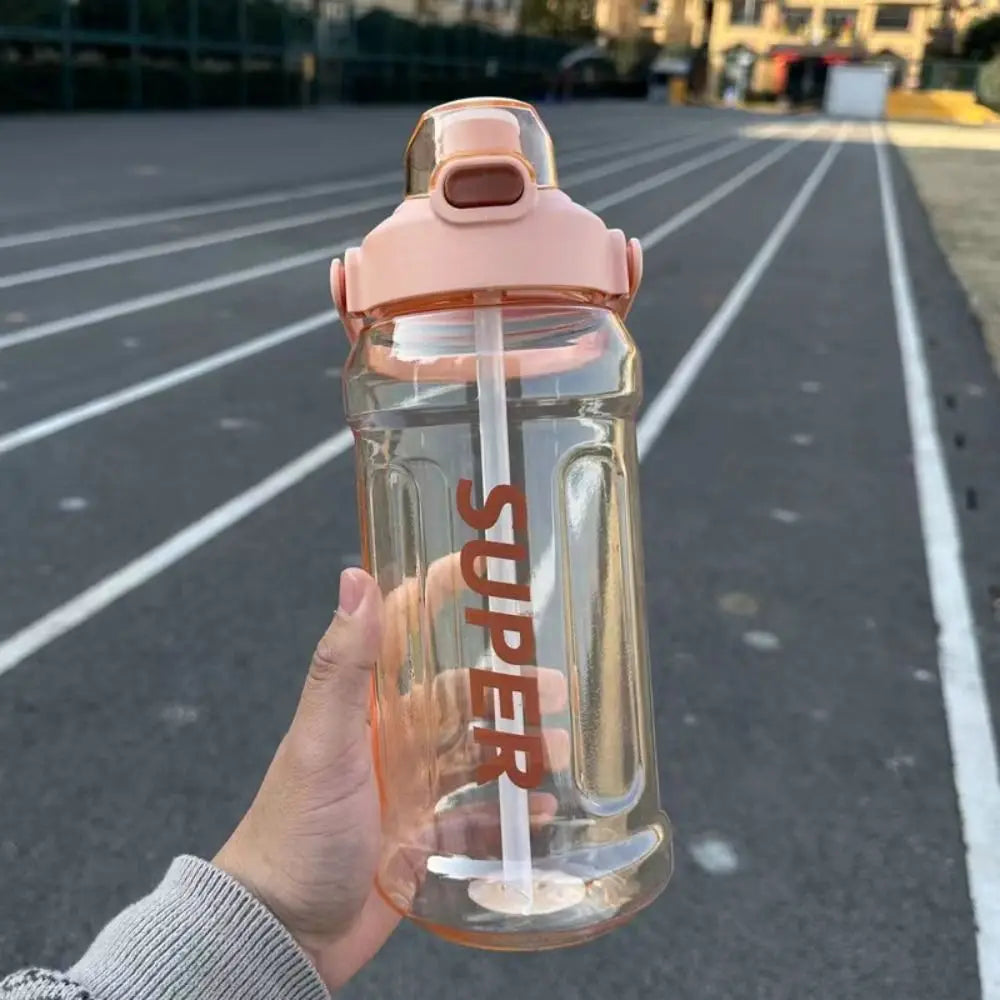 A hand holds a clear, pink insulated sports water bottle with a silicone cap against an asphalt surface.