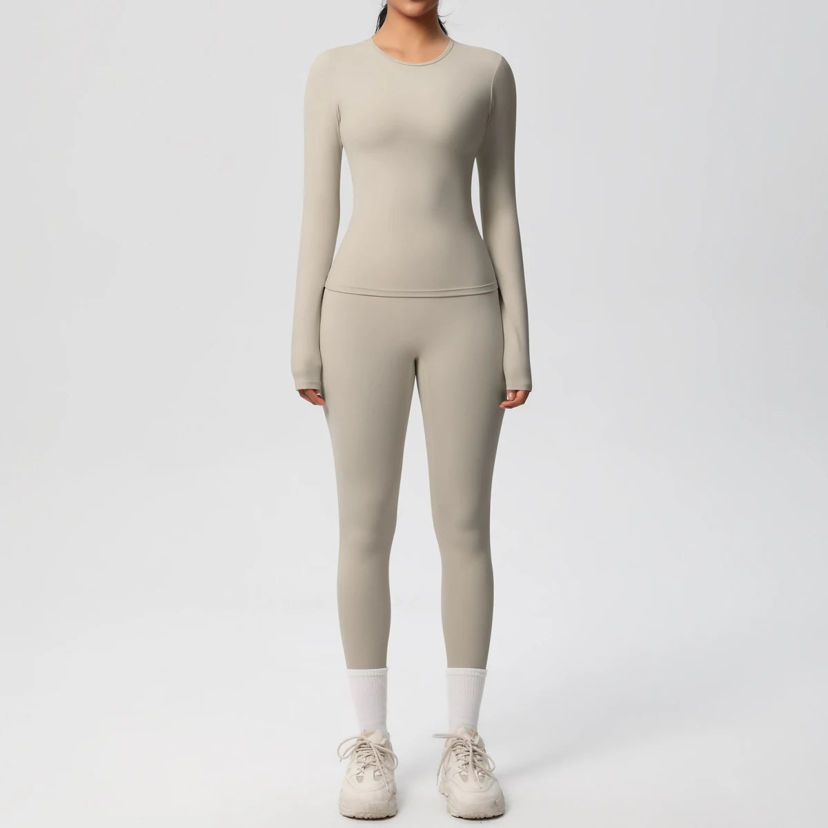 A woman wearing a long-sleeved, fitted beige performance yoga and gym set consisting of a top and matching leggings.