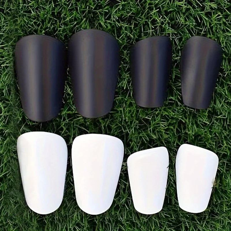 Un jeu de protège-tibias de mini-foot en noir et blanc est exposé sur de l'herbe verte.