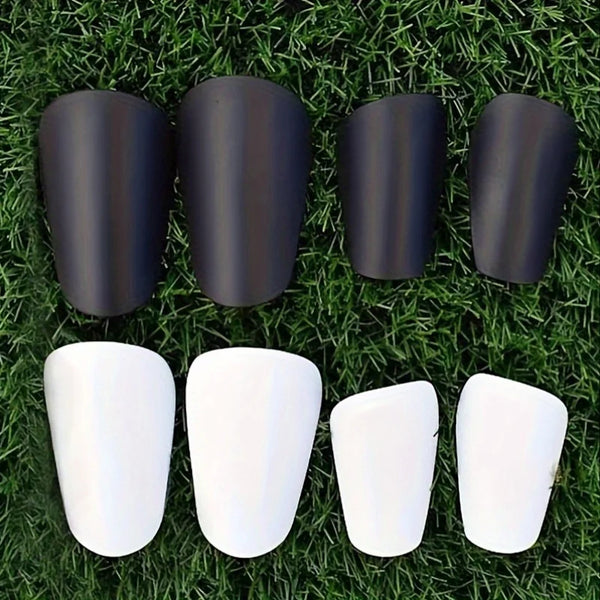 A set of mini soccer shin guards in black and white are displayed on green grass.