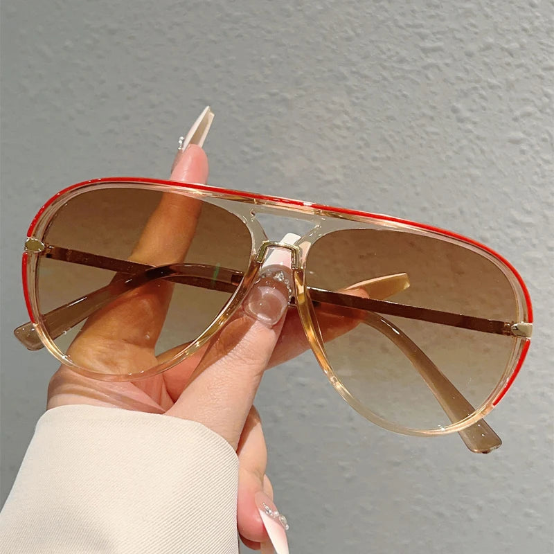 A hand holds a pair of vintage pilot sunglasses with gradient brown lenses and gold-toned frames.