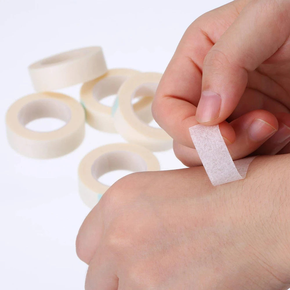 Une main applique du sparadrap médical en papier respirant rose à un poignet.