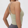 A model wearing a light olive green women's athletic crisscross tank top and gray skirt.