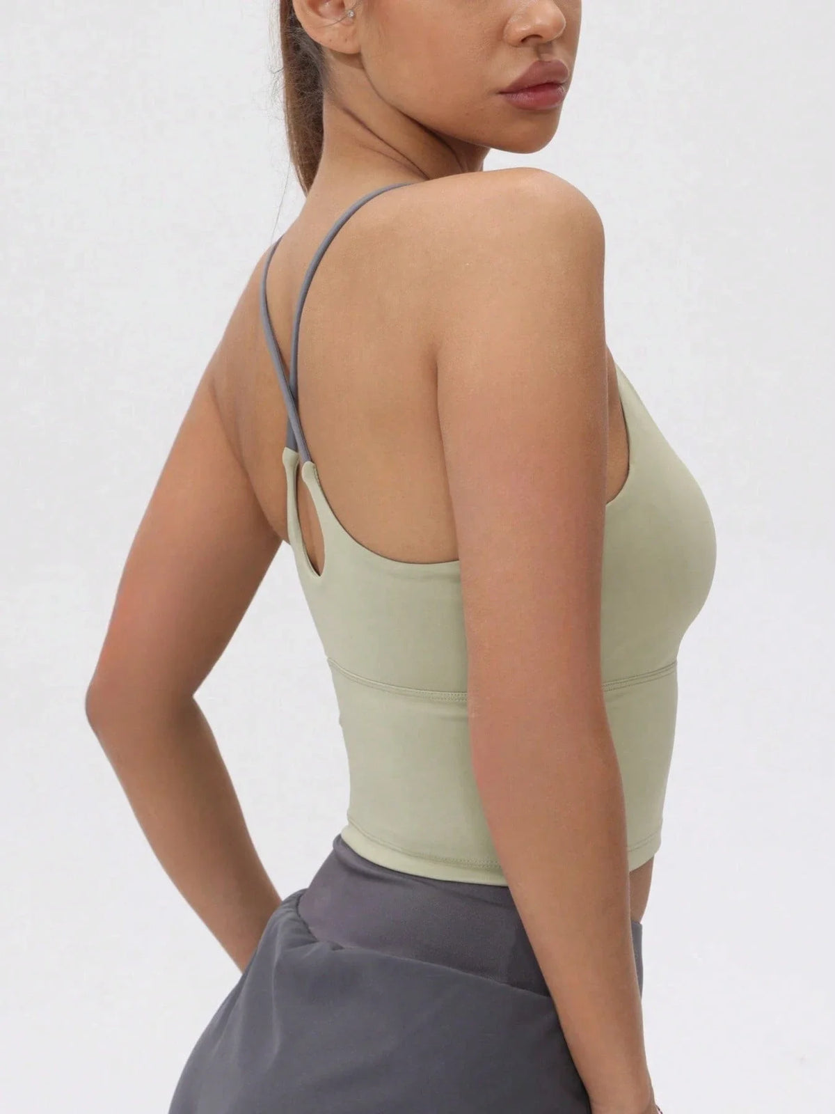 A model wearing a light olive green women's athletic crisscross tank top and gray skirt.