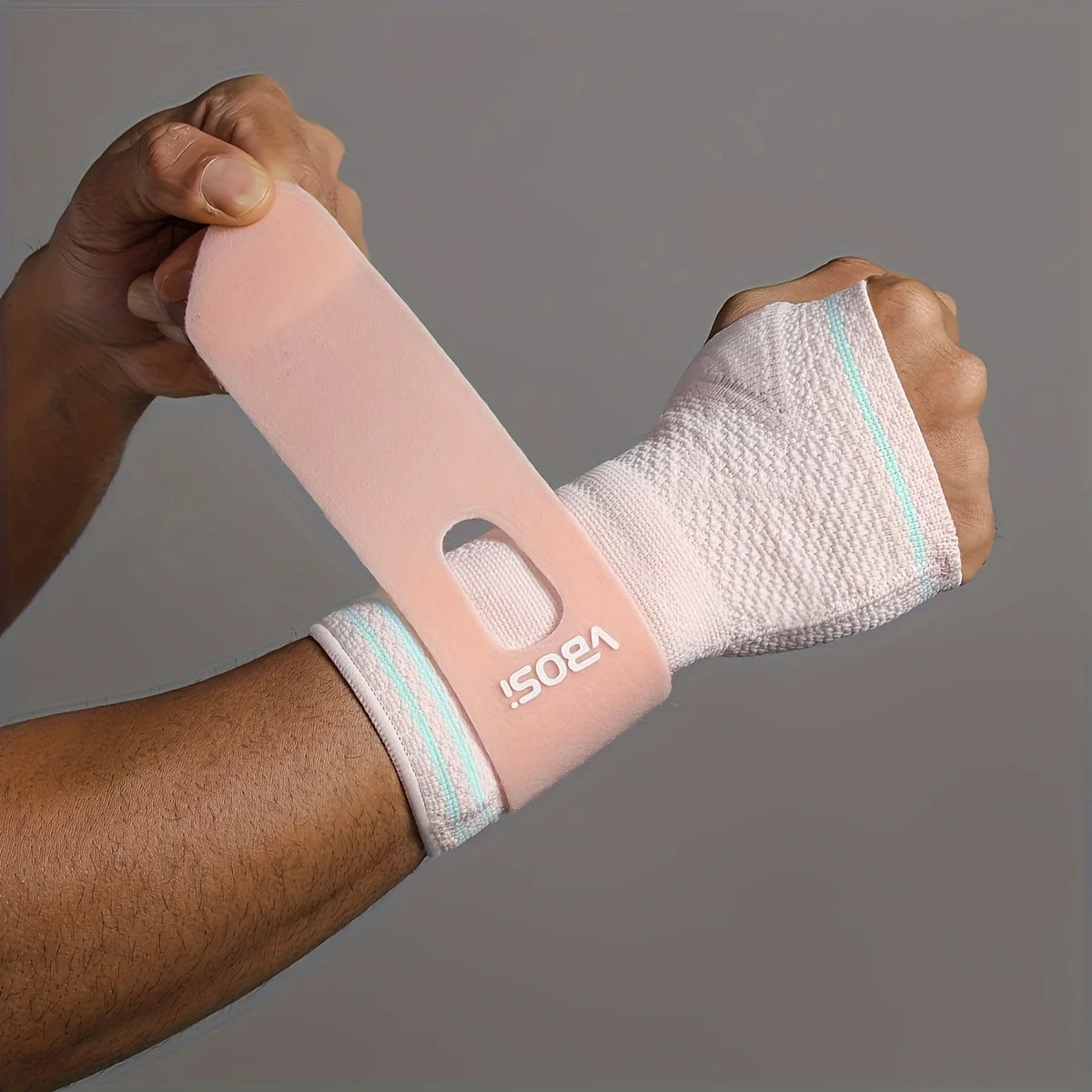 A hand is holding a pink wrist palm support brace on an arm.