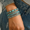 Gros plan d'une main portant cinq bracelets en perles turquoise bohèmes sur le poignet.