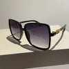 Black sunglasses with a two-tone gradient lens and gold accents resting on a white surface.