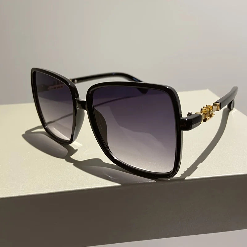 Black sunglasses with a two-tone gradient lens and gold accents resting on a white surface.
