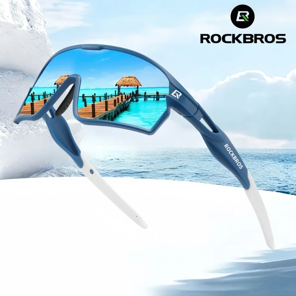 A pair of blue polarized cycling sunglasses with a white temple, shown against a tropical ocean background.