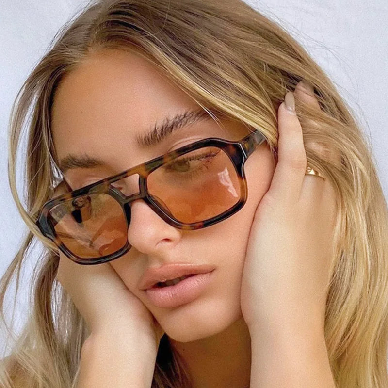 Primer plano de una mujer vistiendo gafas de sol cuadradas tintadas en marrón mientras toca su cabello.