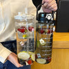 A clear glass water bottle filled with amber liquid and various fruits, held by a person.