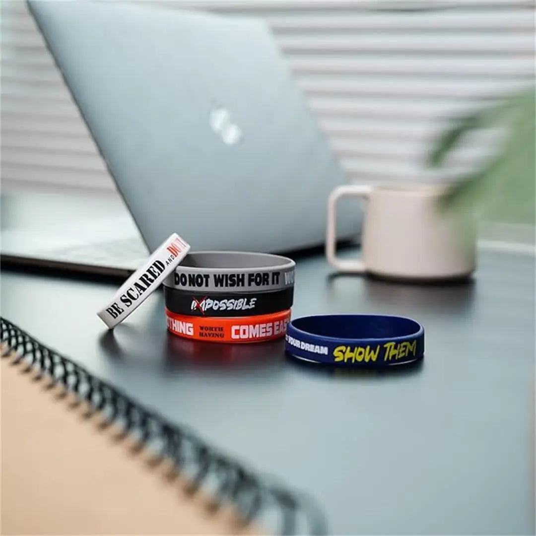 Primer plano de tres pulseras de silicona inspiradoras en negro, rojo y azul sobre una superficie oscura junto a una computad