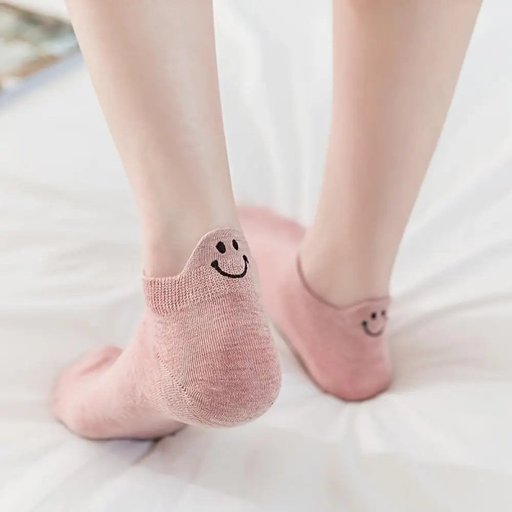 A pair of pink knitted ankle socks with smiling embroidery lying on a white surface.