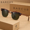 Un par de gafas de sol tortugas marrones sobre una caja de cartón con el logo BARCUR.