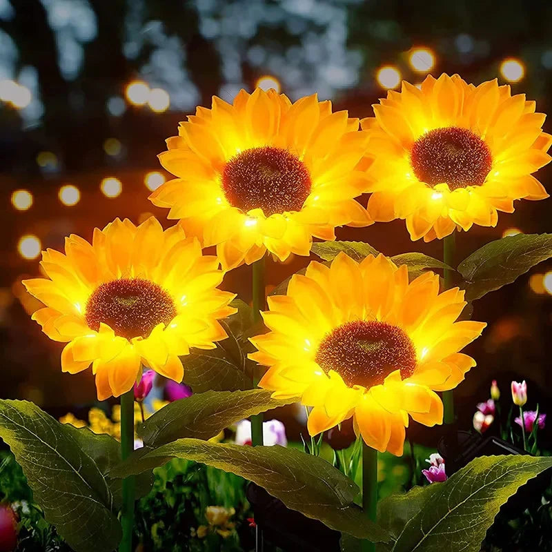 Three bright orange yellow solar sunflower LED stake lights blooming on green foliage.