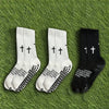 A set of three athletic socks in white and black with a cross print laid on green grass.