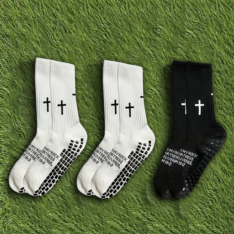 A set of three athletic socks in white and black with a cross print laid on green grass.