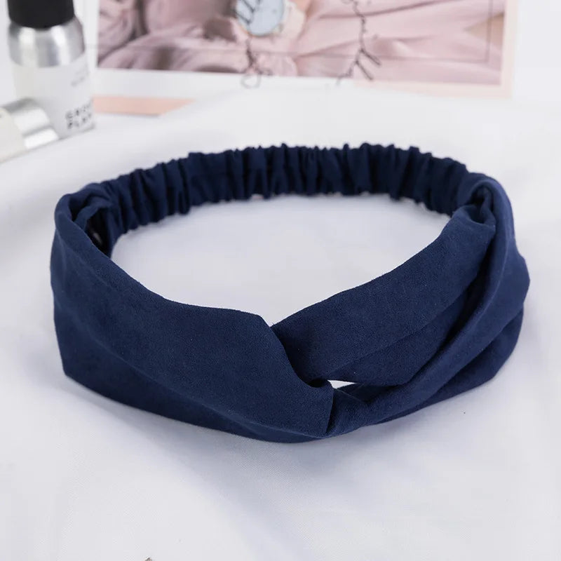 A navy blue fabric headband or hair accessory is shown lying on a white surface.
