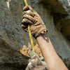 Une main portant des gants sport tactiques agrippe une corde jaune sur un fond rocheux.