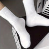 Une paire de chaussettes tubulaires tricotées blanches sur une surface sombre.