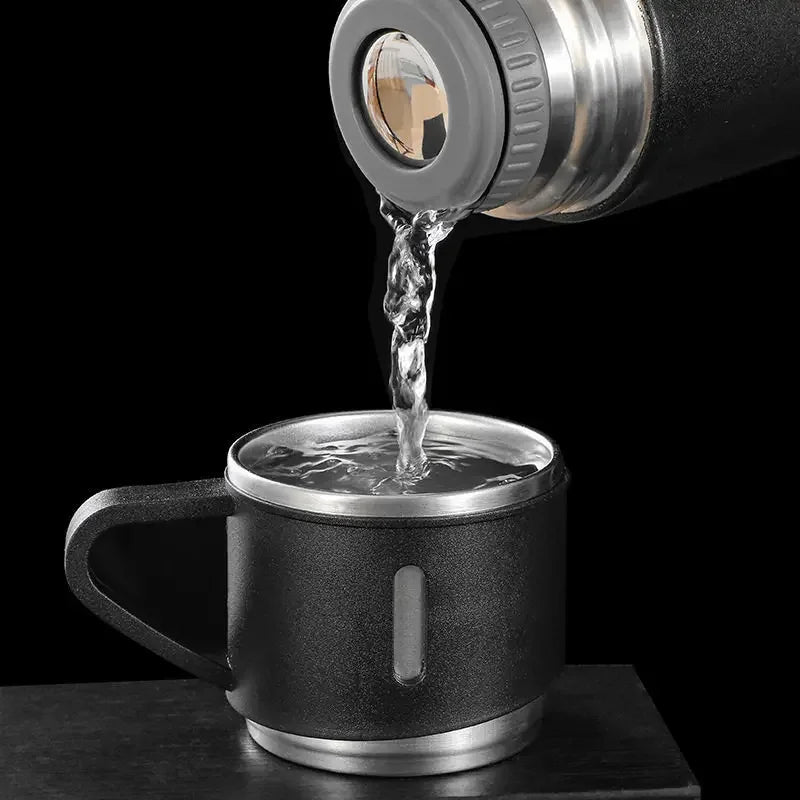 A stainless steel vacuum flask is pouring water into a mug against a black background.