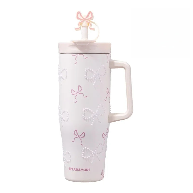 A pink insulated thermos mug with white pearl inlay decoration and a decorative ribbon top.