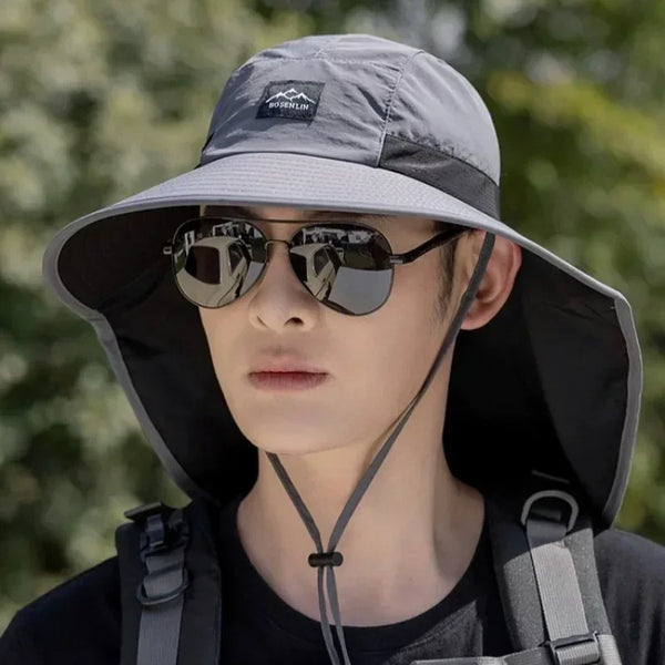 A person wearing a gray wide brim sun hat with a black adjustable neck cover and sunglasses.