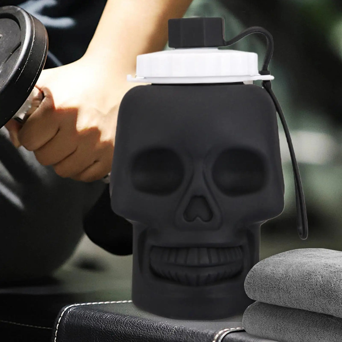 A black skull-shaped leakproof sports water bottle is being held by a hand, resting on a dark surface.