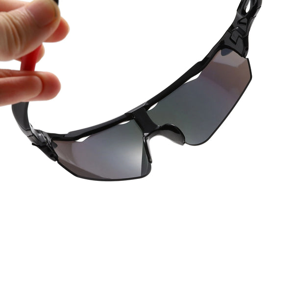 A hand is holding a pair of anti-glare sports sunglasses with dark lenses and black frames.