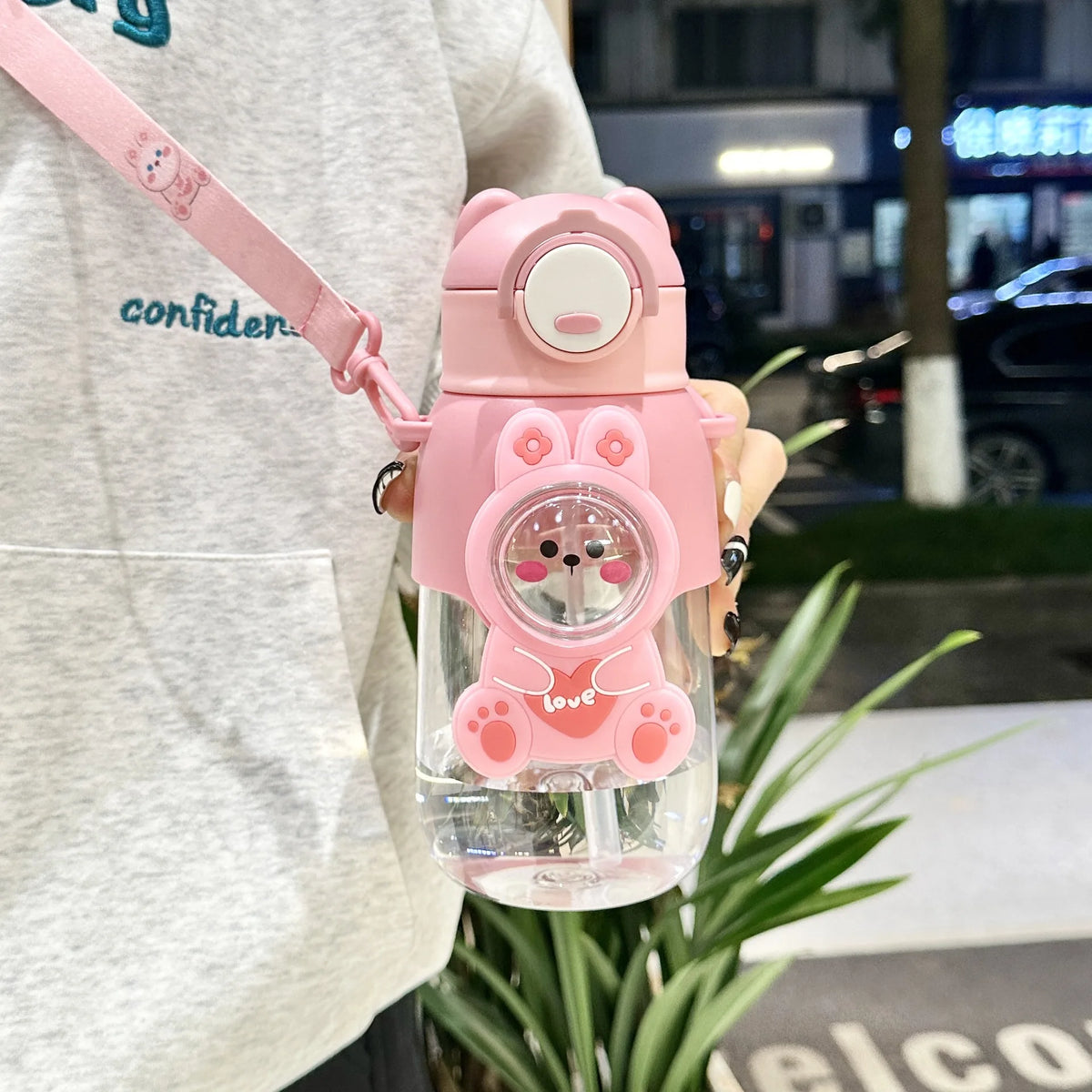 A pink leak-proof water bottle shaped like a cartoon bunny with a pink strap being held by a person.