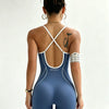 Eine Frau trägt einen dunkelblauen, nahtlosen Yoga-Jumpsuit mit weißen Kreuzrippen und einer goldenen Kettendetail.
