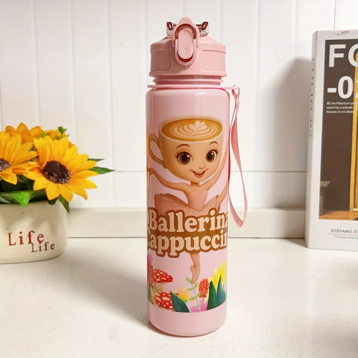 A pink insulated sports water bottle with a cartoon coffee cup design stands on a white surface.