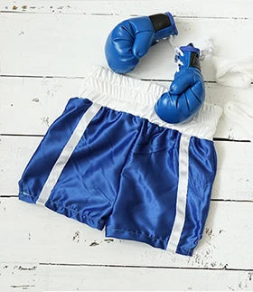 Un par de llaveros de guantes de boxeo azules sobre tela blanca y pantalones cortos deportivos azules.