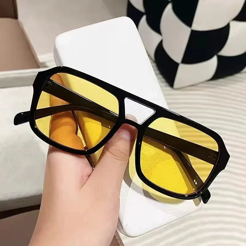 Un par de gafas de sol con montura negra y lentes amarillos sobre una superficie blanca.