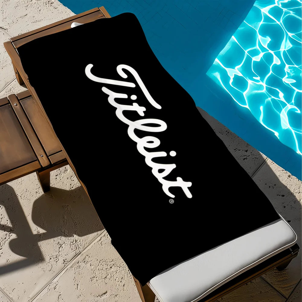A black microfiber beach towel with white text is laid out next to a bright blue swimming pool.