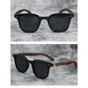 A pair of black sunglasses with brown wood grain frames and polarized lenses resting on a gray textured surface.