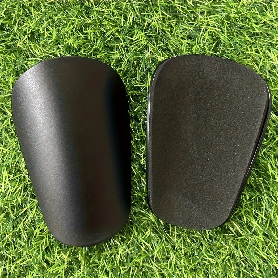 Une paire de genouillères de soccer noires miniatures posées sur de l'herbe verte.