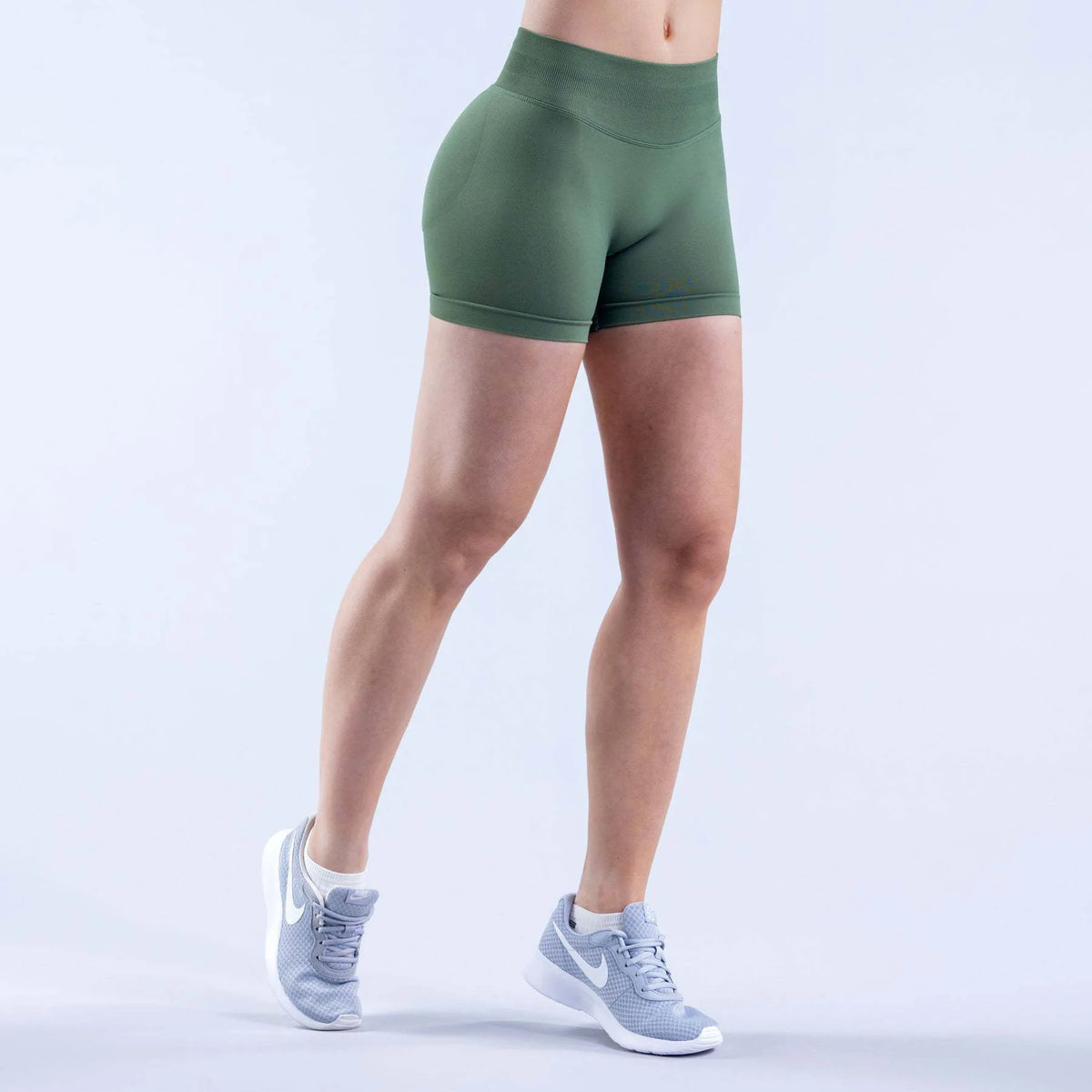 A person wearing olive green seamless high-waisted yoga shorts and white athletic shoes.