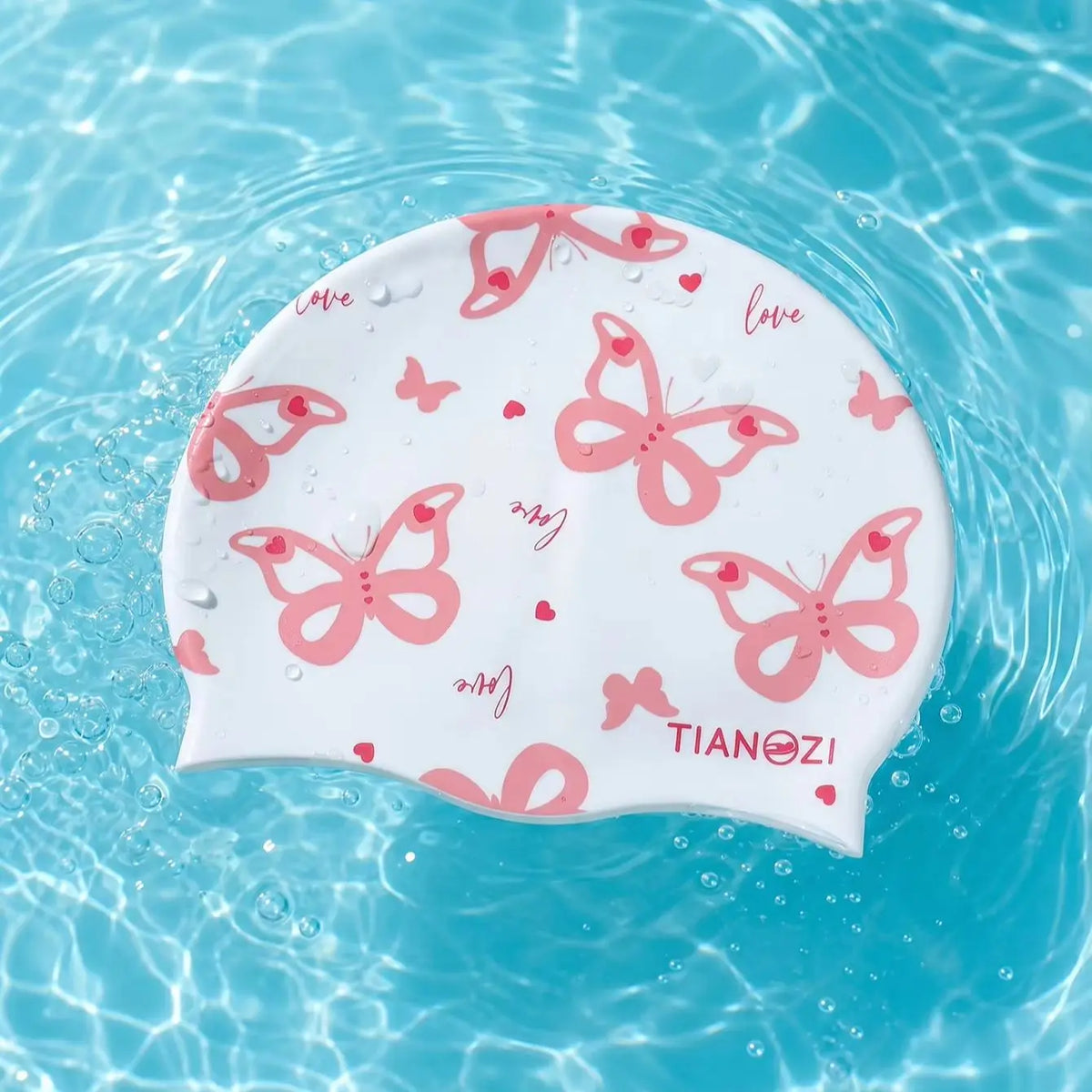 A white silicone swimming cap with a pink butterfly print floating in clear blue water.