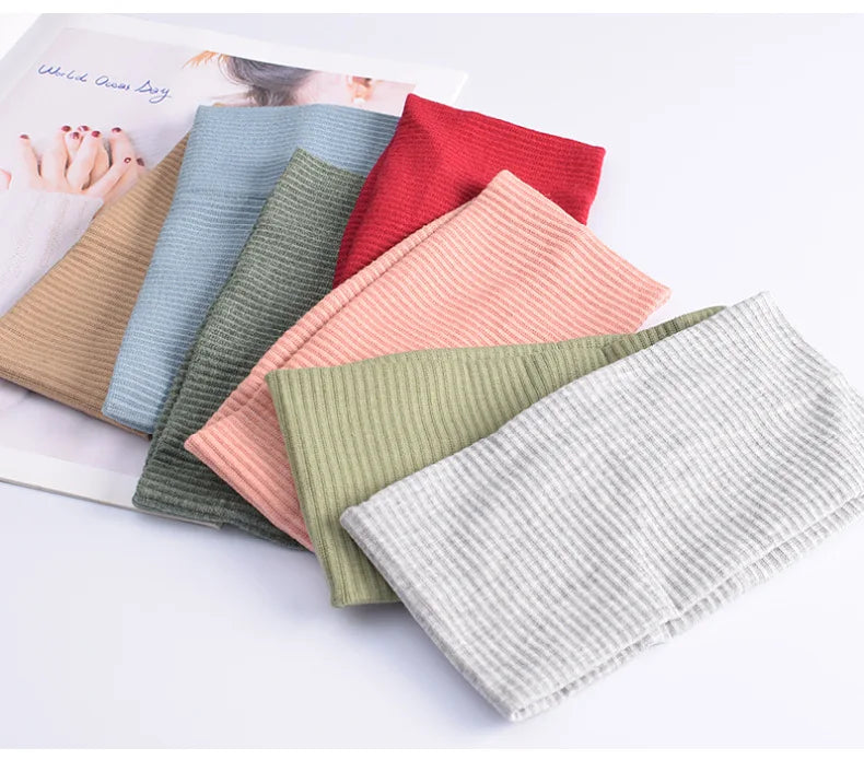 A collection of soft cotton knitted headbands in various pastel and earthy tones laid out on a white surface.