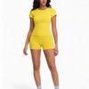 A woman models a yellow two-piece workout set consisting of a short-sleeved top and matching shorts.