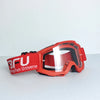 A pair of bright red sport-grade skiing goggles with a clear lens resting on a light gray surface.