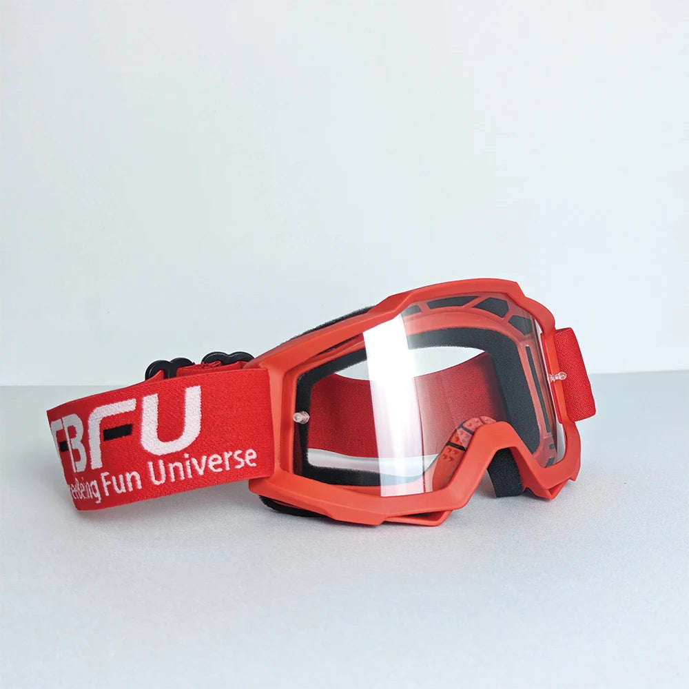 A pair of bright red sport-grade skiing goggles with a clear lens resting on a light gray surface.