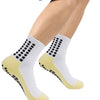 Ein Paar weiße sportliche Grip-Socken mit schwarzen Punkten und gelben Akzenten auf einem Fuß.