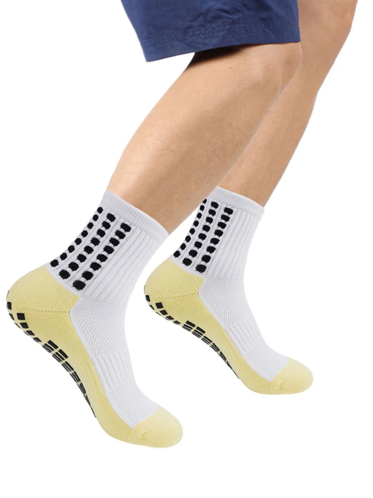 Ein Paar weiße sportliche Grip-Socken mit schwarzen Punkten und gelben Akzenten auf einem Fuß.