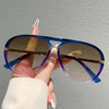 A hand holds a pair of vintage pilot sunglasses with blue gradient lenses and gold accents.