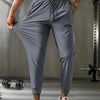 A muscular man models gray breathable casual jogger pants in a gym setting.
