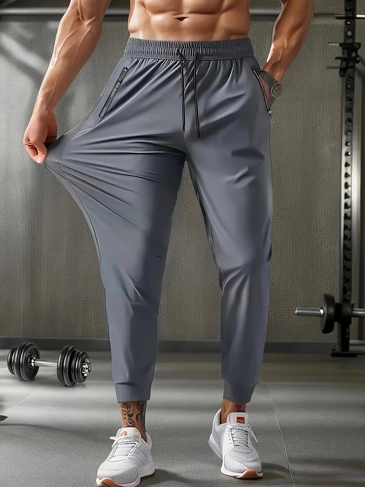 A muscular man models gray breathable casual jogger pants in a gym setting.